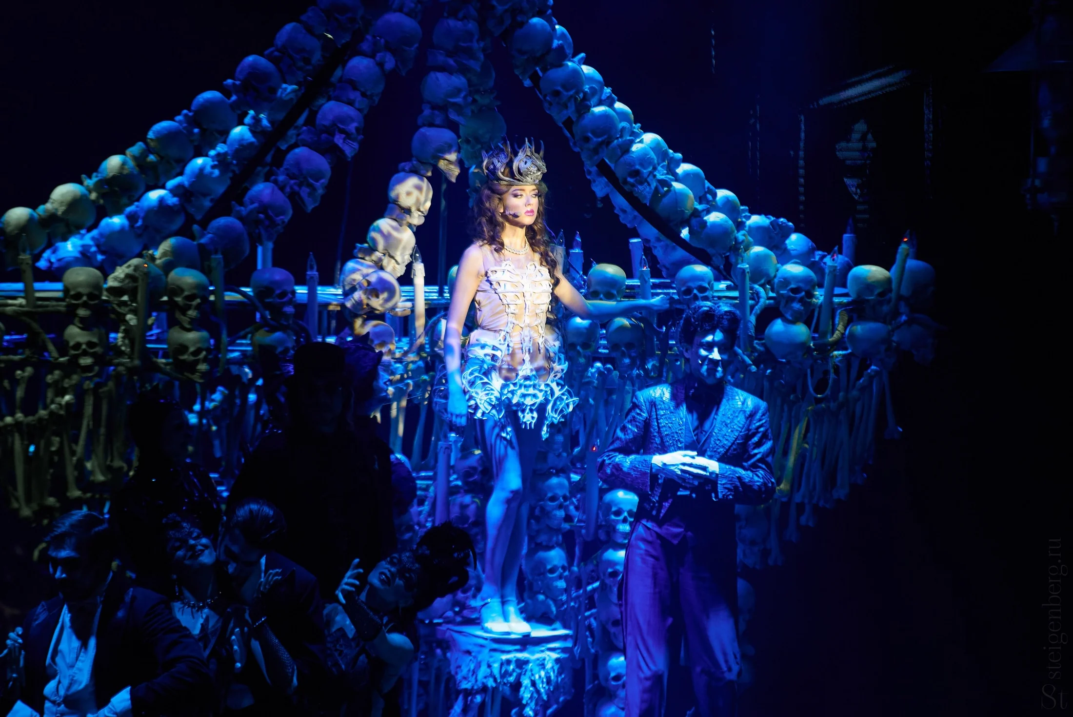 Large ensemble scene under cold blue theatrical light